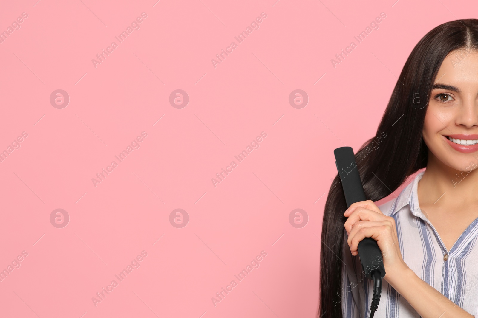 Photo of Beautiful happy woman using hair iron on pink background, closeup. Space for text