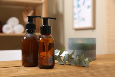 Dispensers of liquid soap, burning candle and eucalyptus branch on bath tray indoors. Space for text