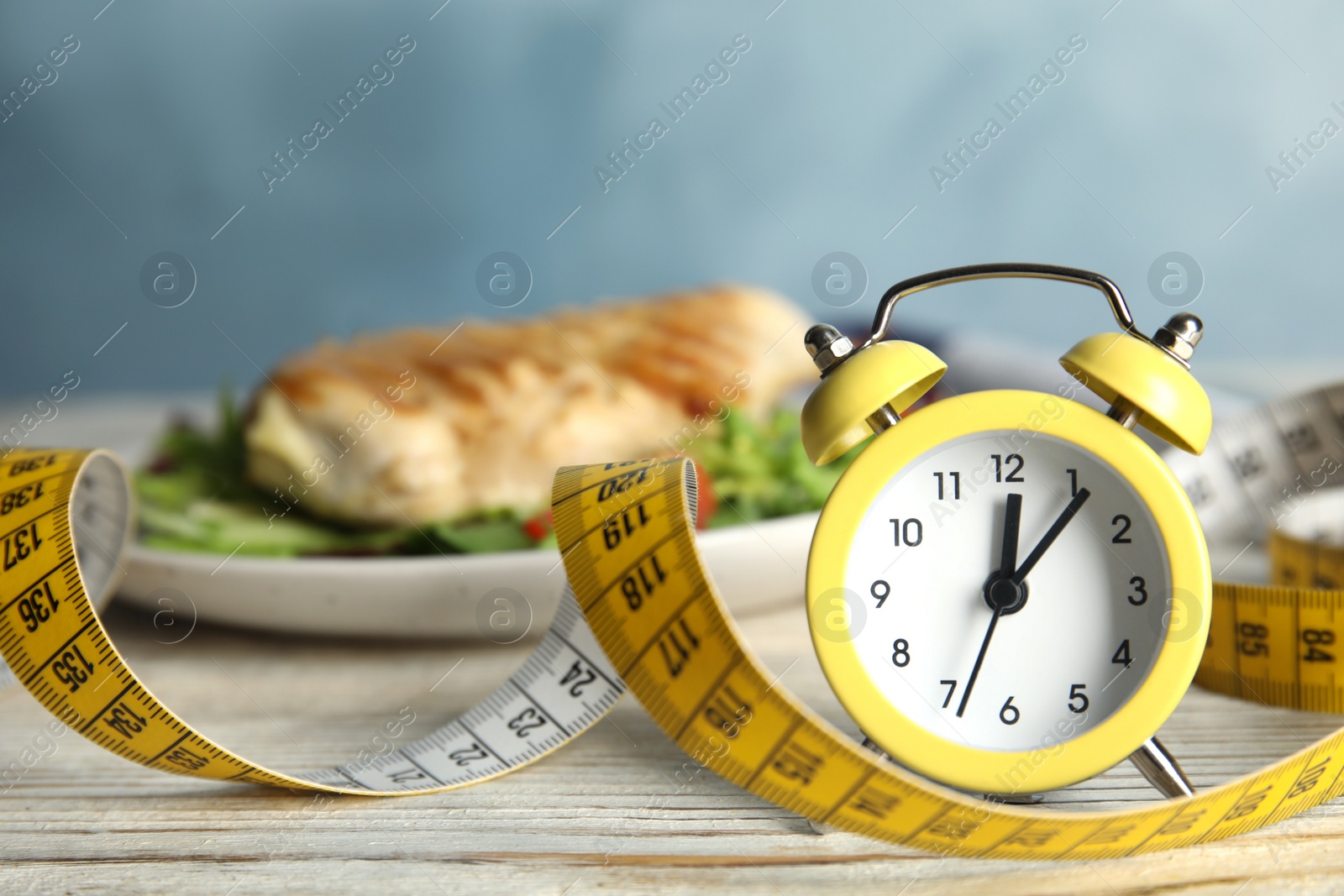 Photo of Alarm clock and measuring tape on white wooden table. Diet regime