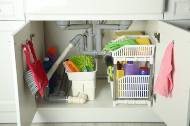 Photo of Different cleaning tools and supplies in open cabinet under sink