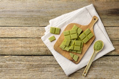 Pieces of tasty matcha chocolate bar and powder in spoon on wooden table, top view. Space for text