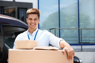Photo of Young courier with parcels near delivery car outdoors