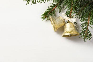 Photo of Christmas bells and fir tree branches on white wooden table, flat lay. Space for text