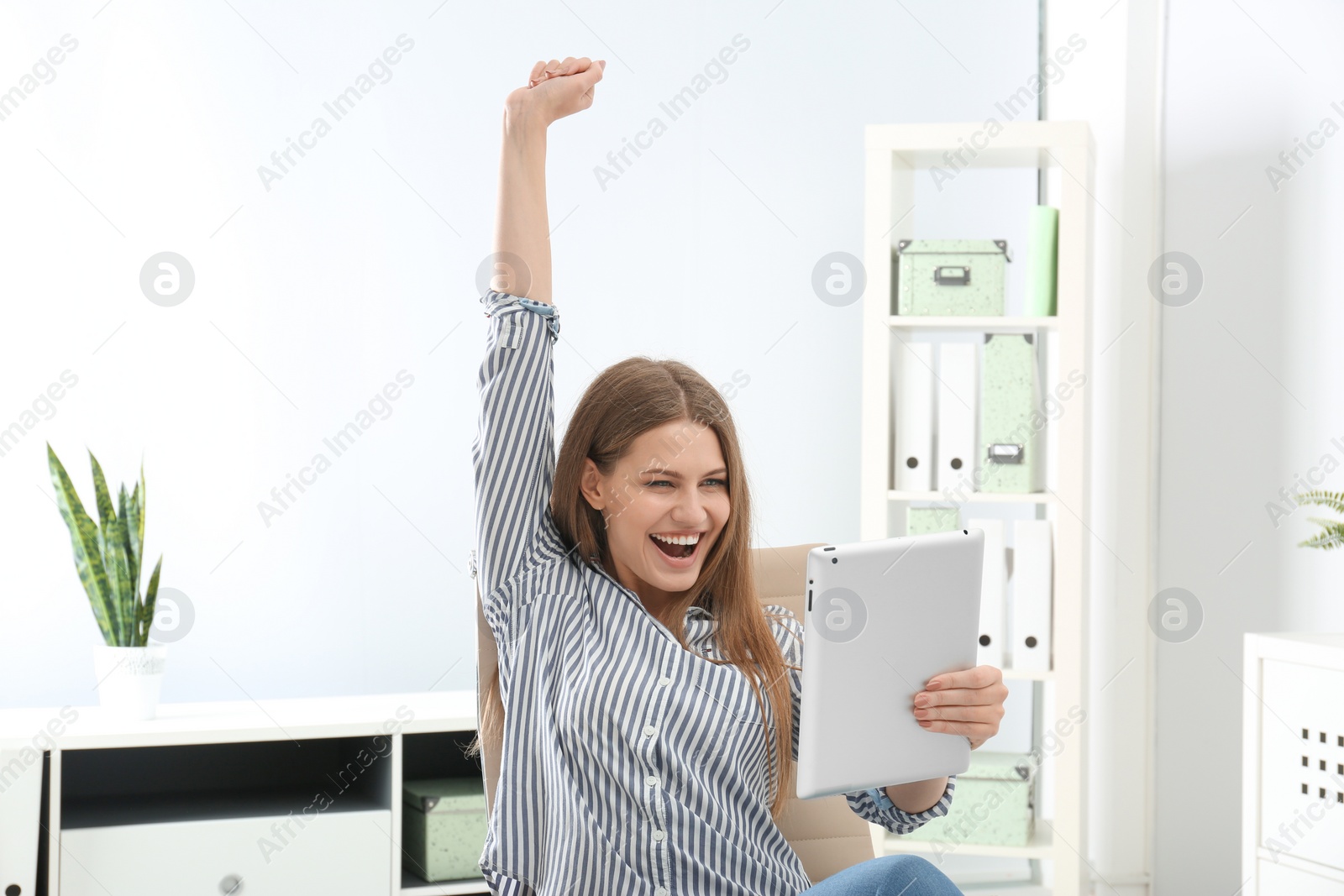 Photo of Emotional young woman with tablet celebrating victory in office