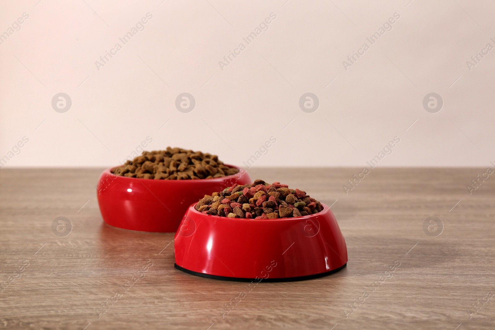 Photo of Dry food in red pet bowls on wooden surface