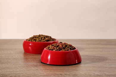 Photo of Dry food in red pet bowls on wooden surface