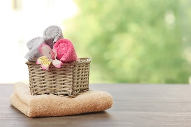 Photo of Basket and fresh towels with flower on wooden table, space for text
