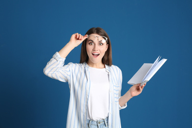 Emotional young woman with book on blue background