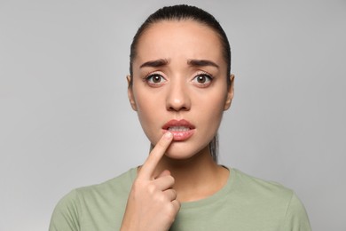 Emotional woman with herpes touching lips on light grey background