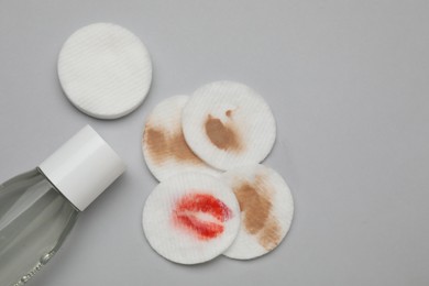 Photo of Bottle of makeup remover, clean and dirty cotton pads on light grey background, flat lay. Space for text