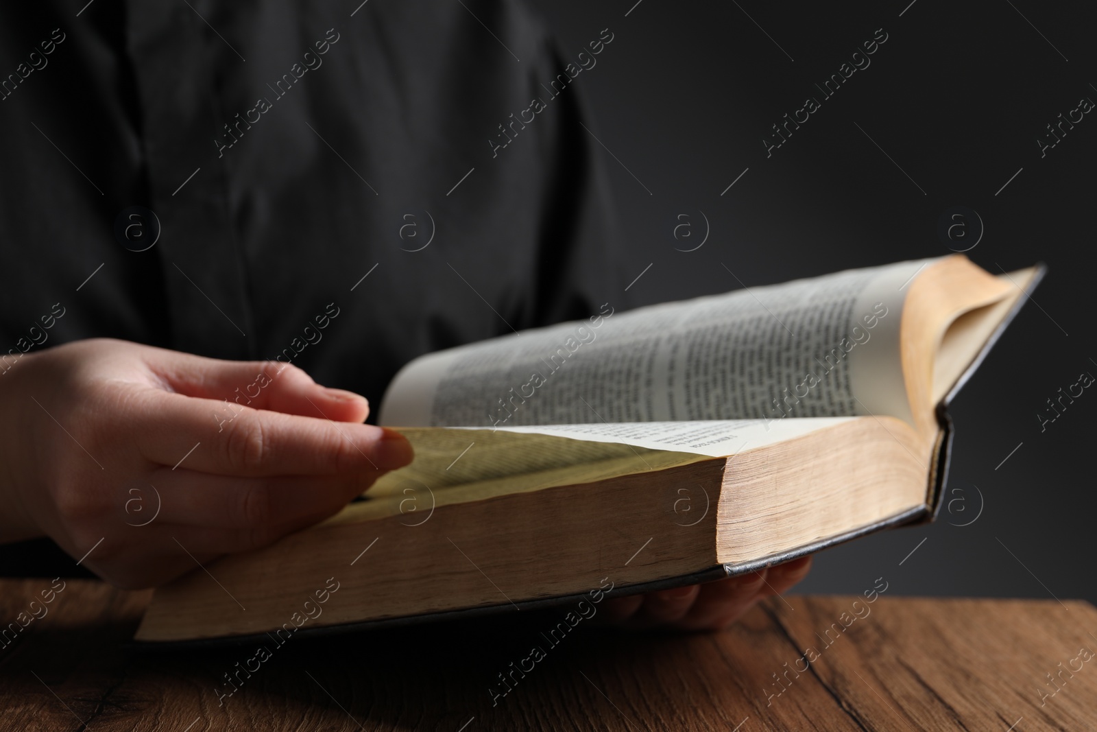 Photo of Woman reading Bible at wooden table, closeup