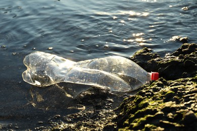 Photo of Used plastic bottle near water outdoors. Environment pollution