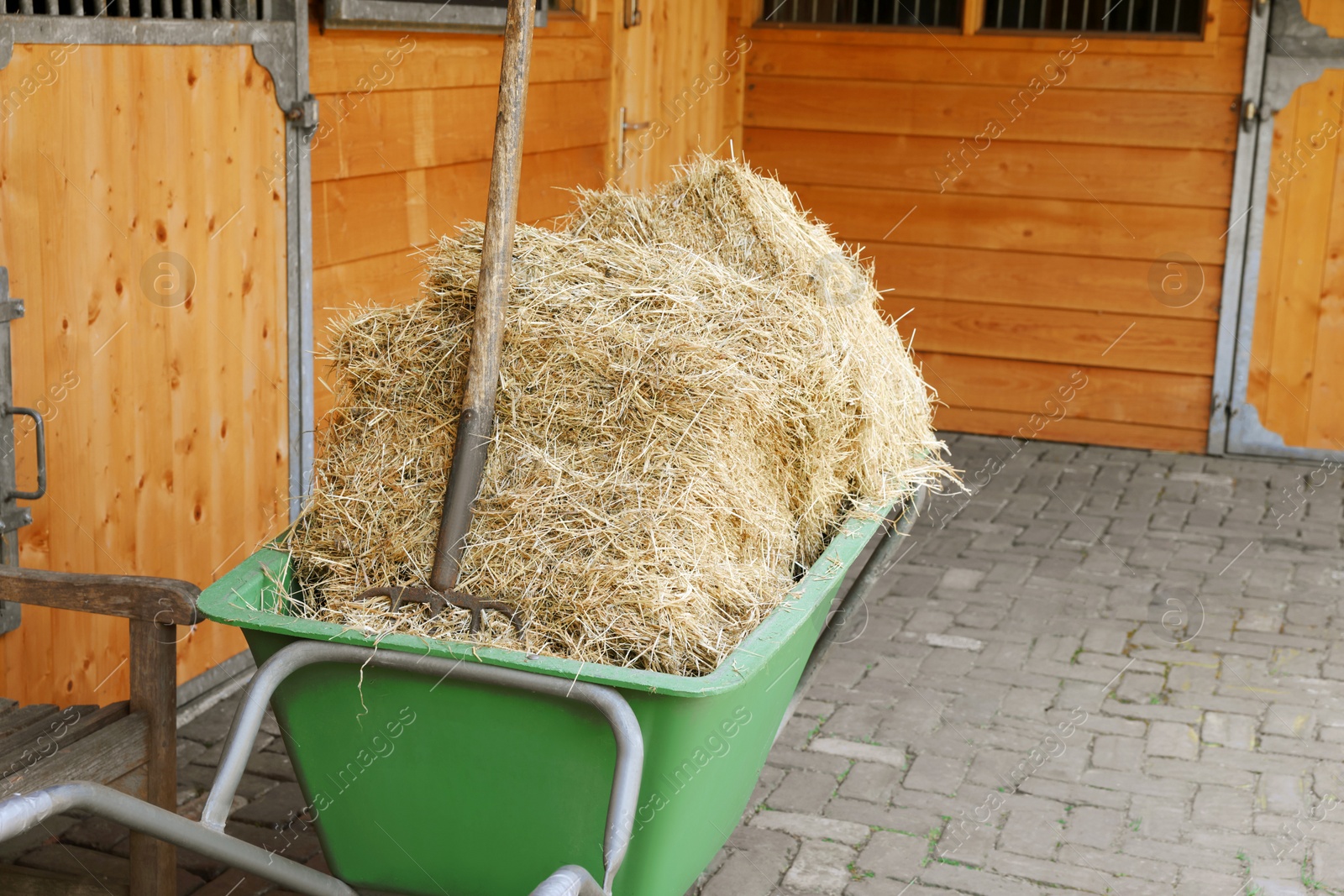 Photo of Wheelbarrow with hay near wooden stable outdoors