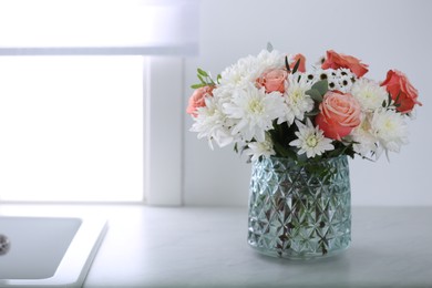Vase with beautiful flowers on countertop in kitchen, space for text. Interior design