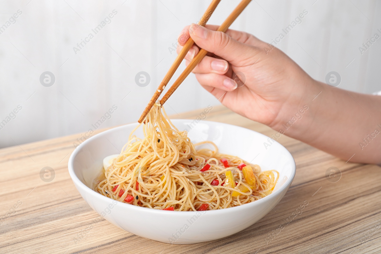 Photo of Woman eating cooked Asian noodles with chopsticks at table, closeup