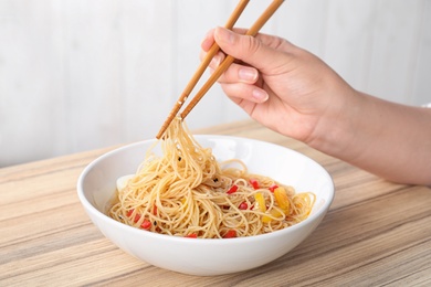 Photo of Woman eating cooked Asian noodles with chopsticks at table, closeup