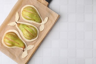 Board with raw dough and fresh pears on white tiled table, top view. Space for text