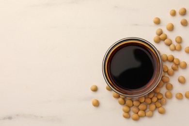 Soy sauce in bowl and soybeans on white marble table, flat lay. Space for text