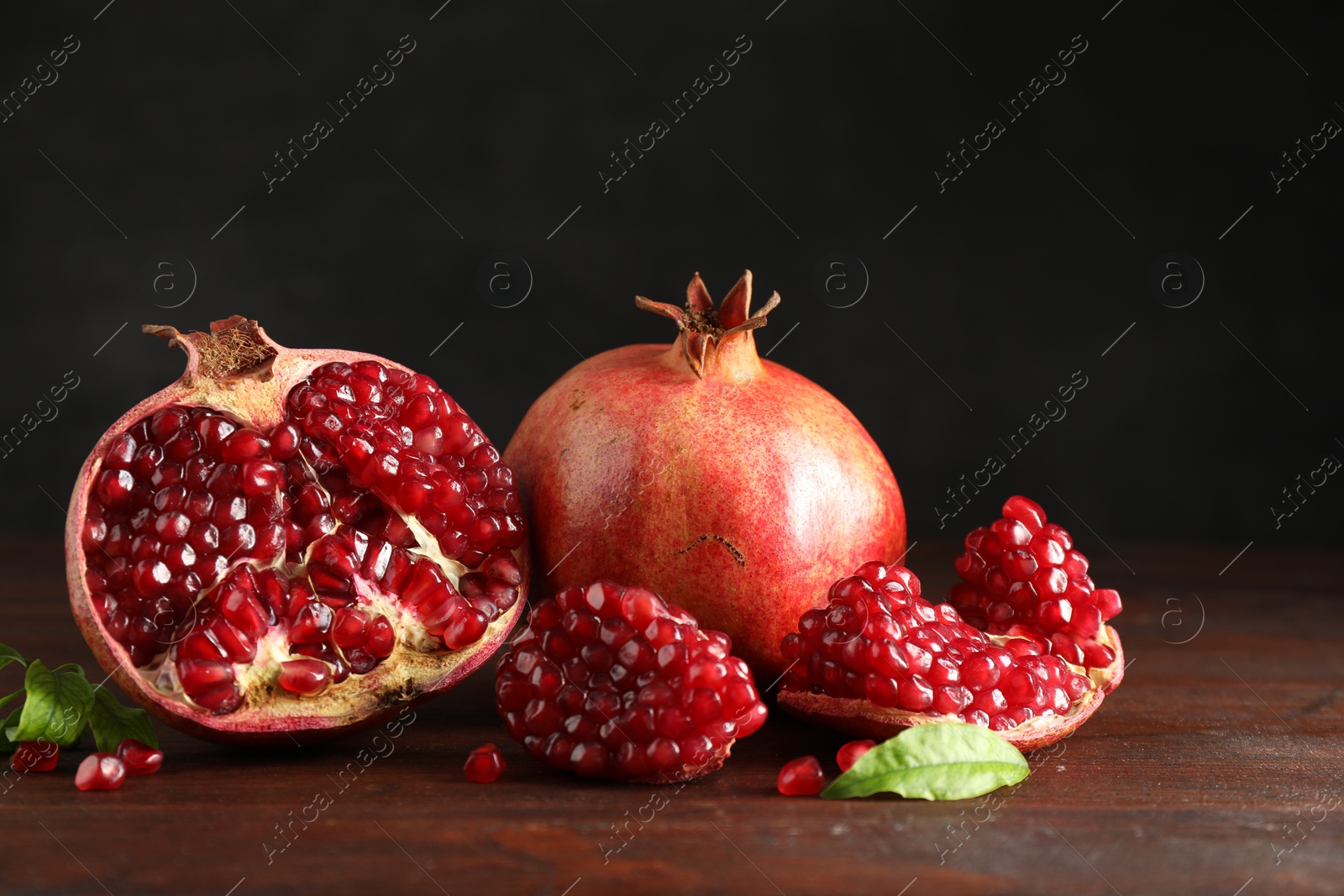 Photo of Fresh pomegranates and green leaves on wooden table