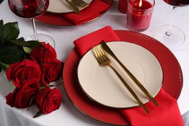 Place setting with roses and candle on white table. Romantic dinner