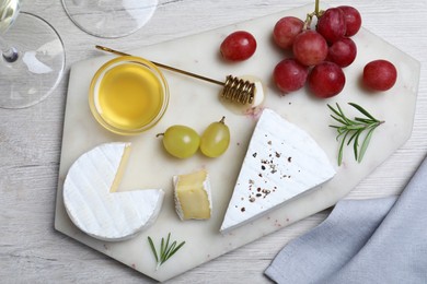 Photo of Tasty brie cheese with honey, rosemary and grapes on white wooden table, flat lay