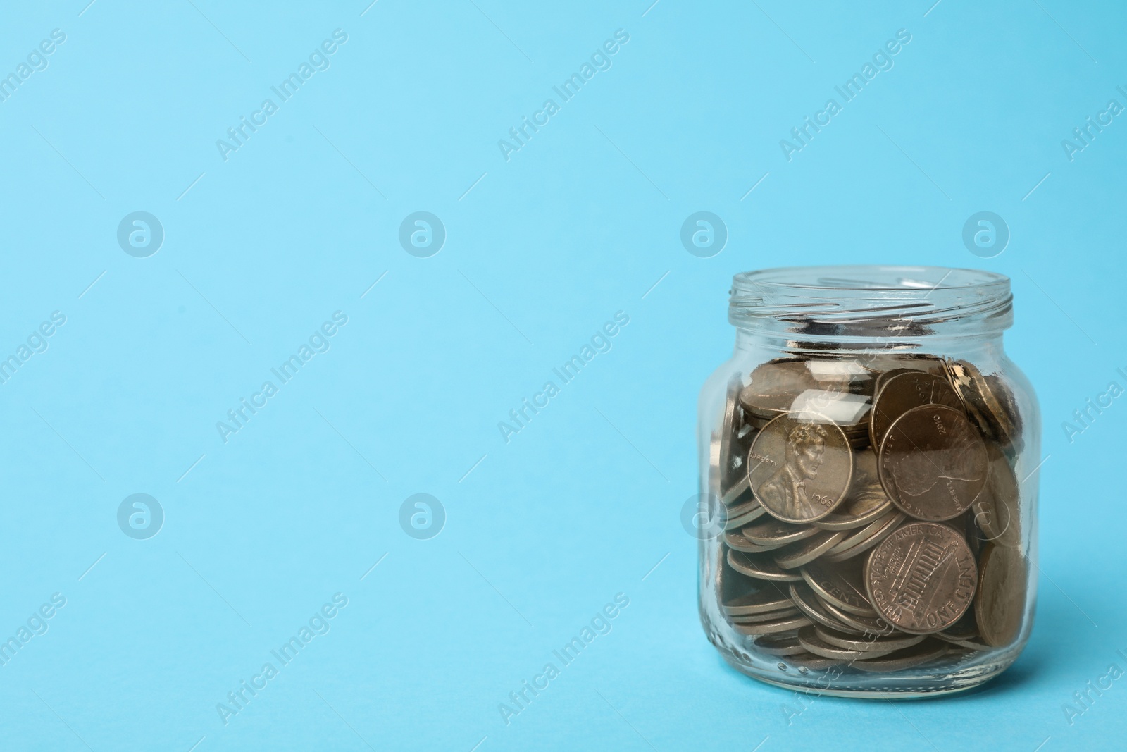 Photo of Glass jar with coins on light blue background, space for text