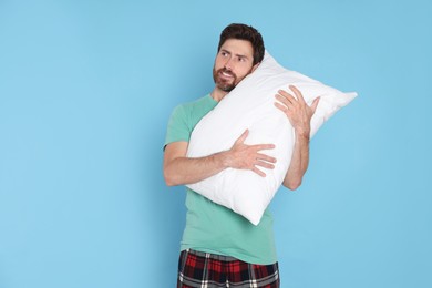 Photo of Smiling handsome man hugging soft pillow on light blue background, space for text