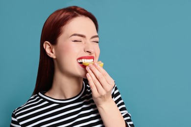 Photo of Woman with red dyed hair eating lemon on light blue background, space for text