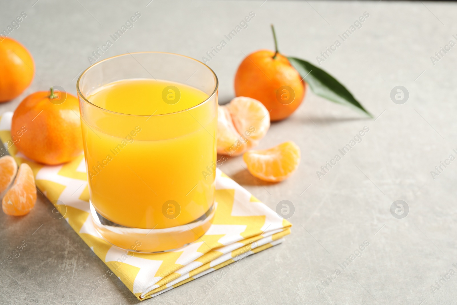 Photo of Glass of fresh tangerine juice and fruits on light grey table. Space for text