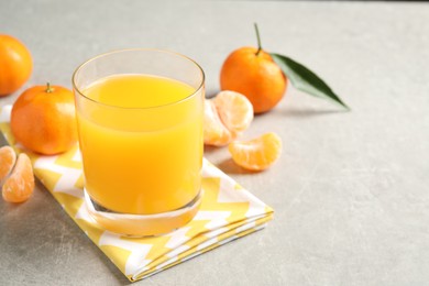 Glass of fresh tangerine juice and fruits on light grey table. Space for text