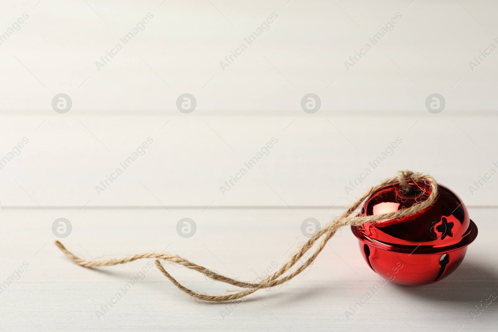Photo of Red sleigh bell with rope on white wooden table. Space for text