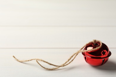 Red sleigh bell with rope on white wooden table. Space for text