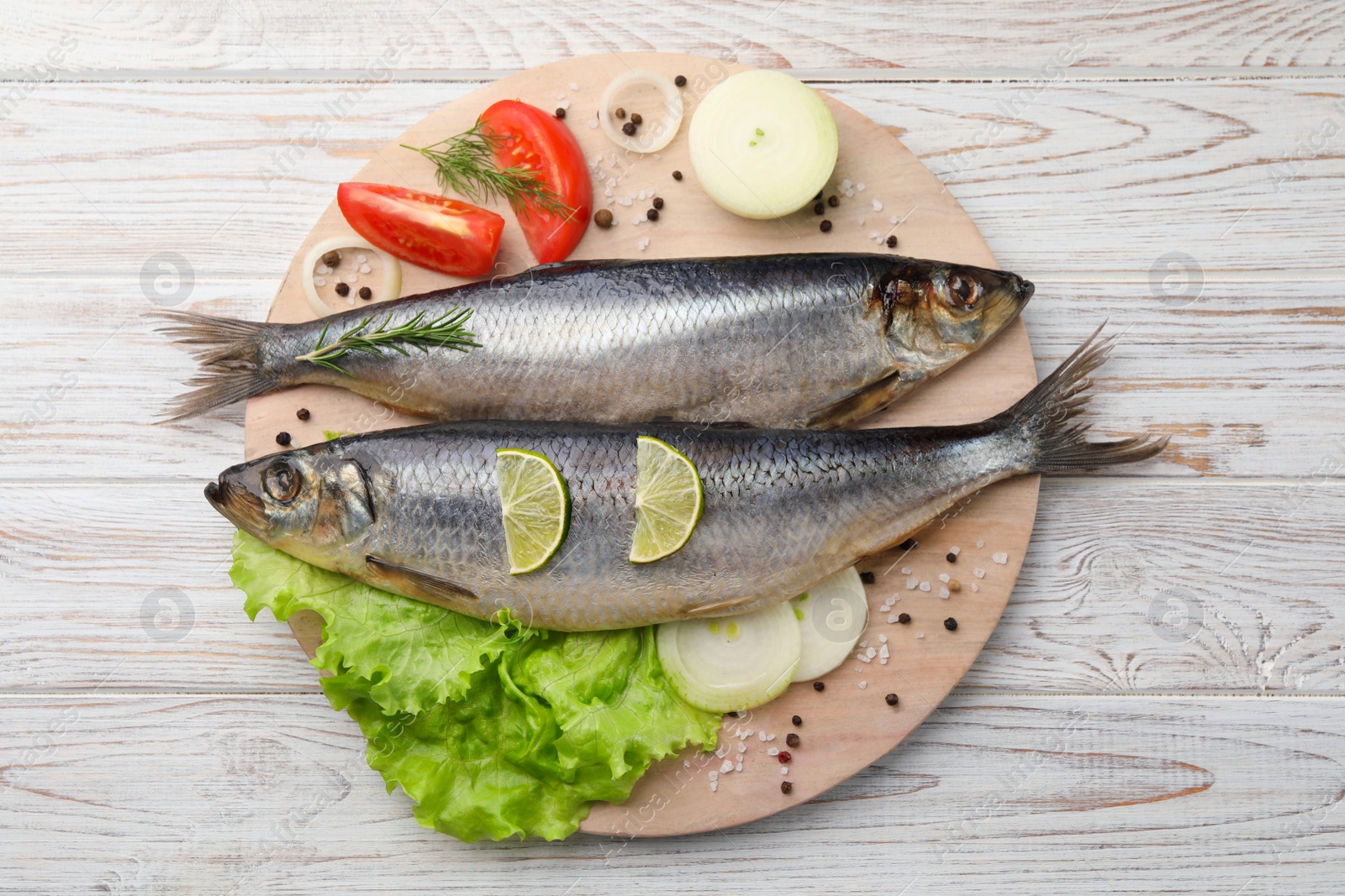 Photo of Board with delicious salted herrings and ingredients on white wooden table, top view