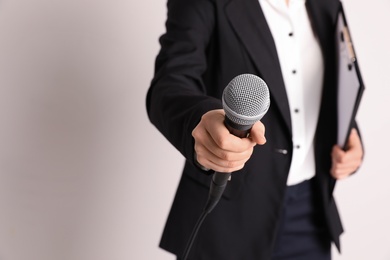 Photo of Young businesswoman holding microphone and clipboard on color background. Space for text