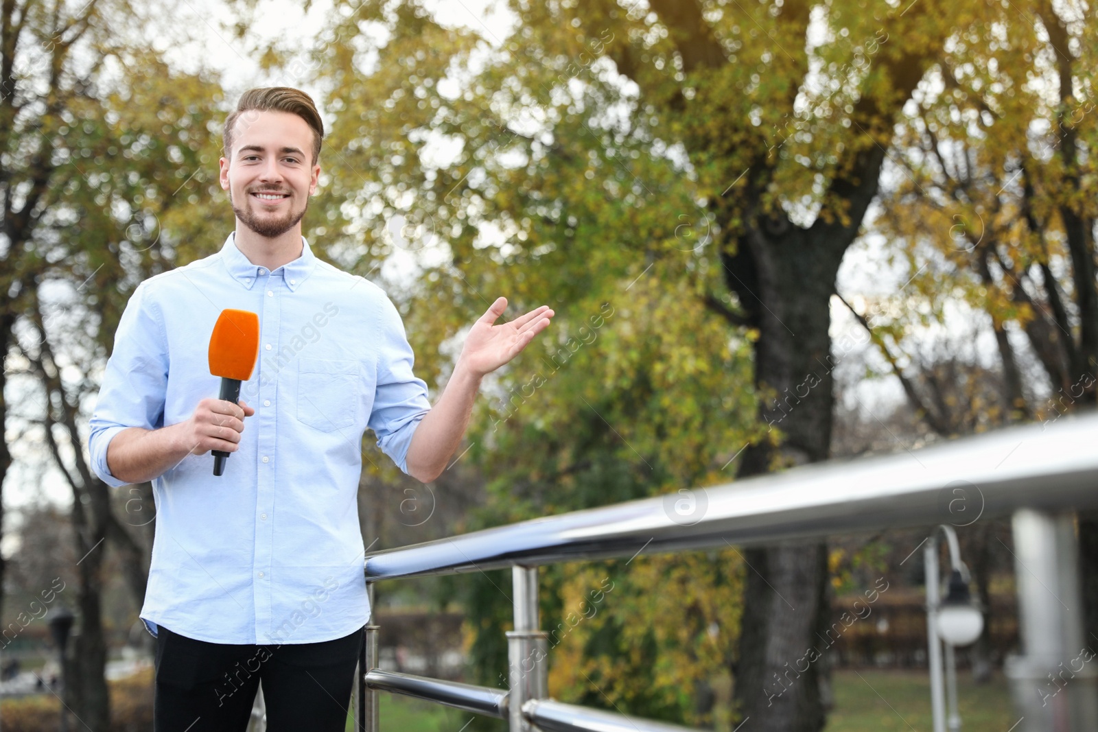 Photo of Young male journalist with microphone working in park. Space for text