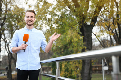 Young male journalist with microphone working in park. Space for text
