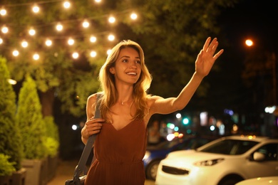 Photo of Young woman catching taxi on city street at night