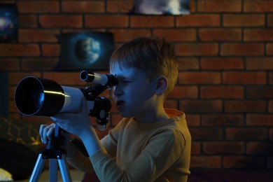 Little boy looking at stars through telescope in room