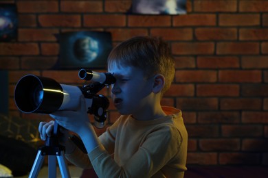 Photo of Little boy looking at stars through telescope in room