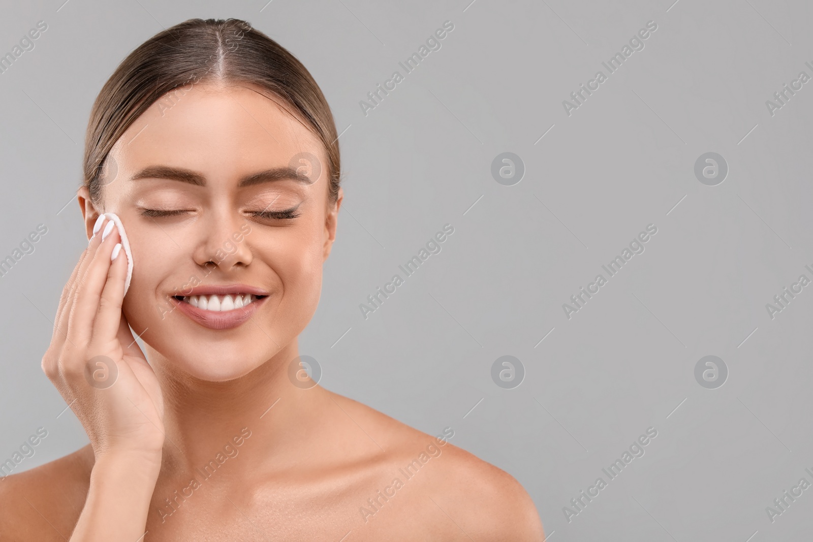 Photo of Beautiful woman removing makeup with cotton pad on grey background, space for text