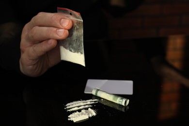 Photo of Drug addiction. Man with cocaine and rolled dollar banknote at black table, closeup