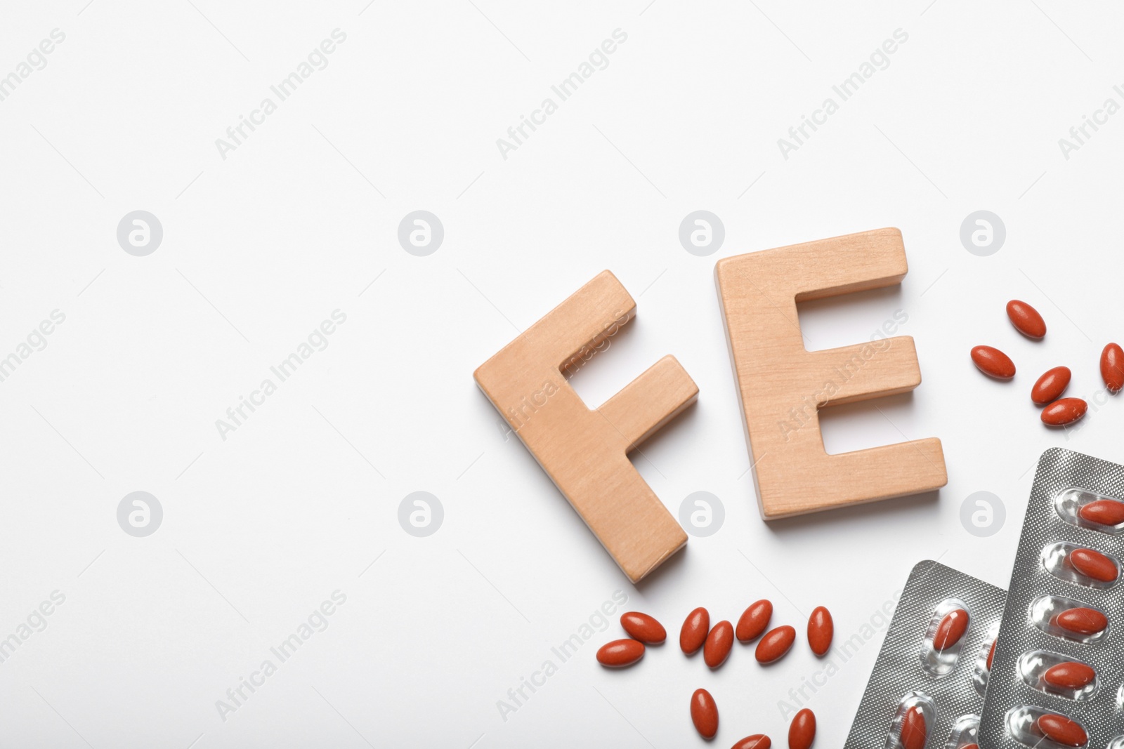 Photo of Wooden letters FE and pills on white background, top view. Anemia concept