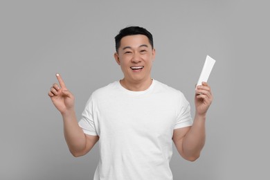 Photo of Handsome man with tube of body cream on light grey background