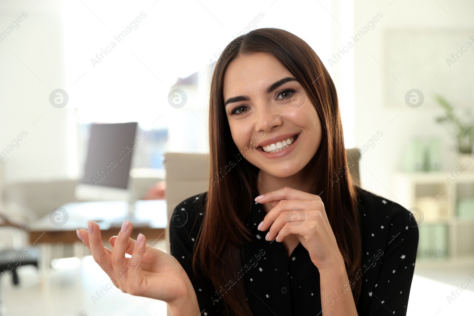 Photo of Young woman looking at camera and using video chat in home office