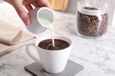 Woman pouring milk into cup with aromatic coffee at white marble table, closeup