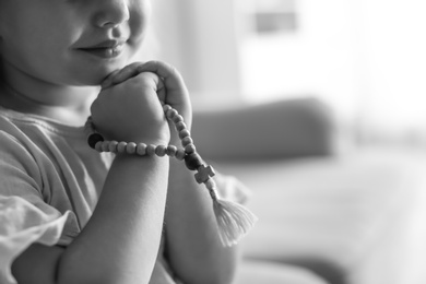 Photo of Cute little girl with beads praying indoors, black and white effect. Space for text