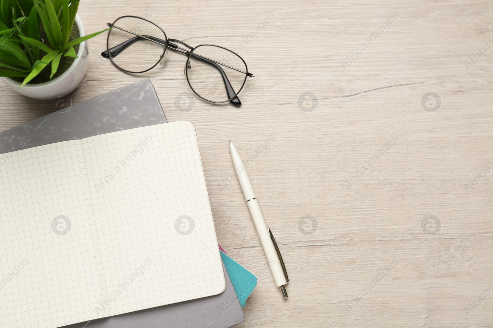 Photo of Notebooks, pen, glasses and plant on wooden table, flat lay. Space for text