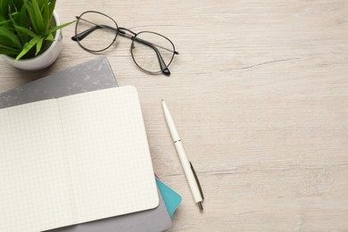 Photo of Notebooks, pen, glasses and plant on wooden table, flat lay. Space for text