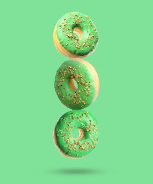 Tasty donuts with sprinkles falling on light green background