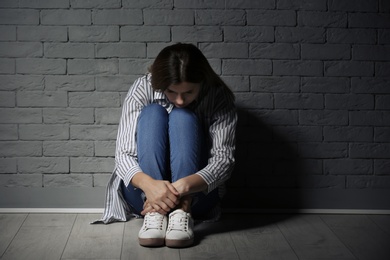 Lonely woman suffering from depression near brick wall